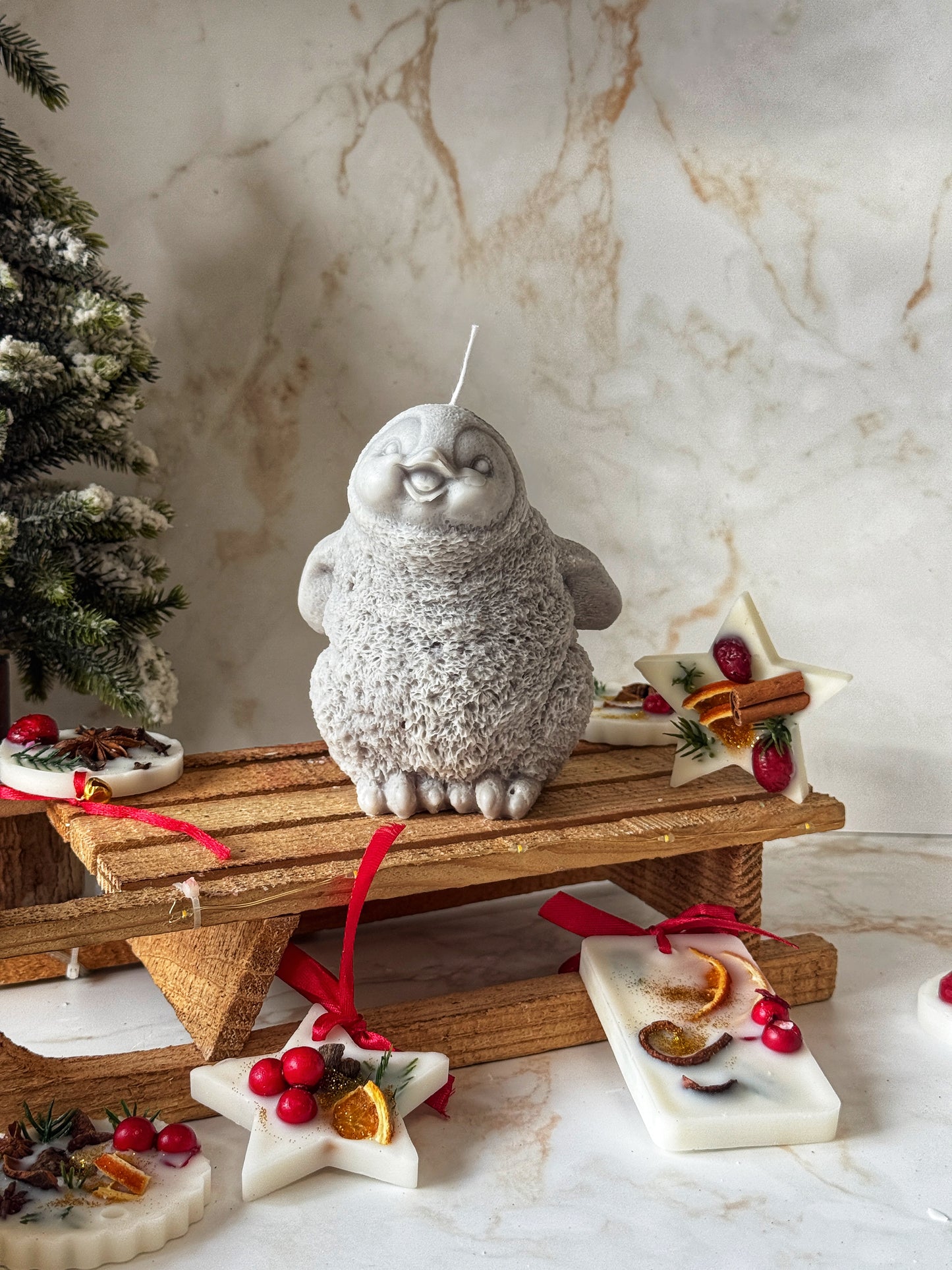 Decorative candle shaped like a gray creature on a wooden stand with Christmas decorations.