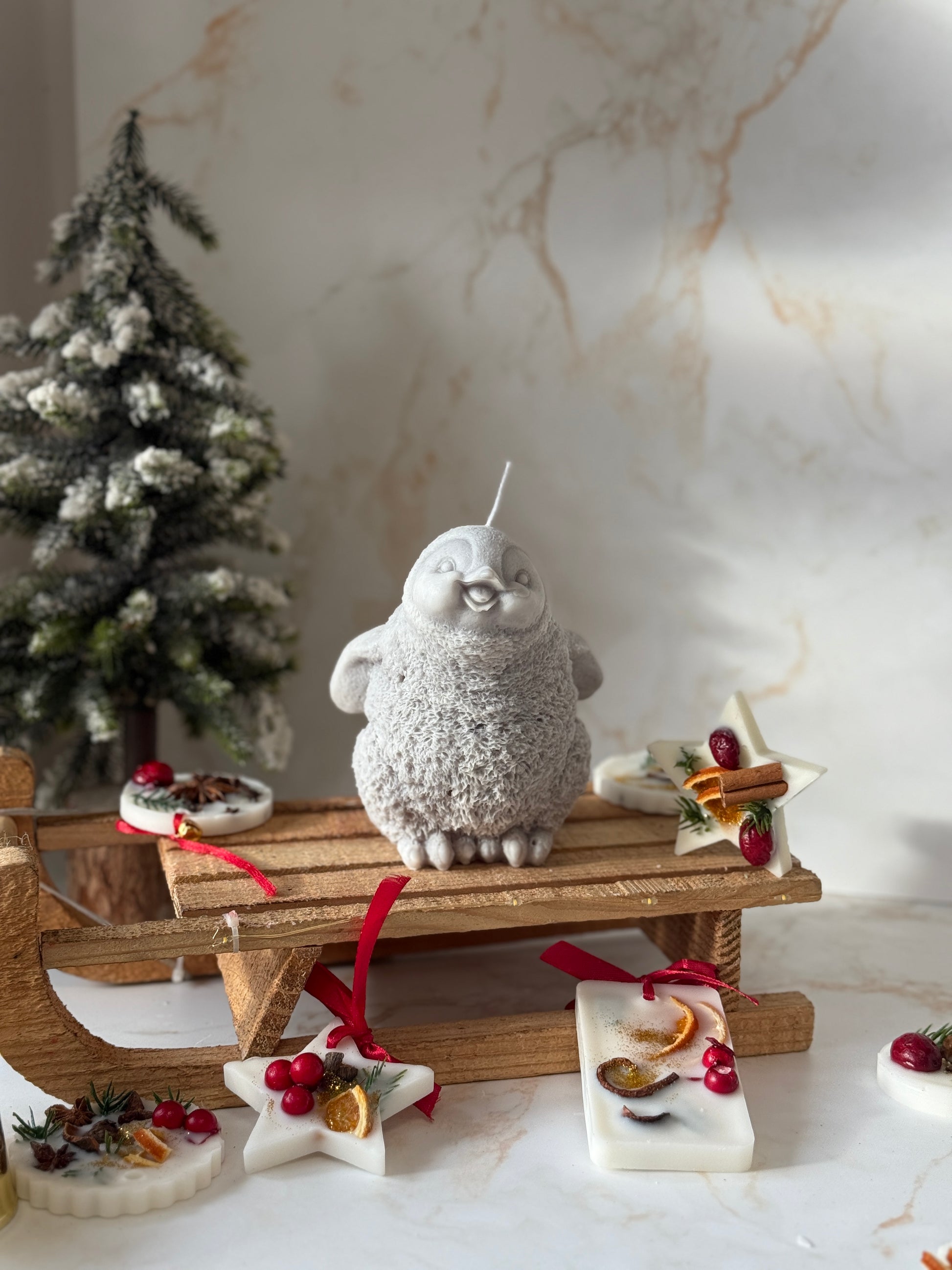 Decorative penguin on a small wooden sled with Christmas decorations against a marble wall.