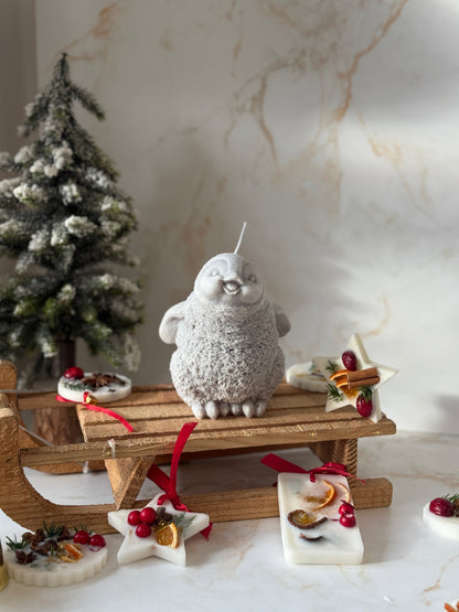 Decorative penguin on a small wooden sled with Christmas decorations against a marble wall.