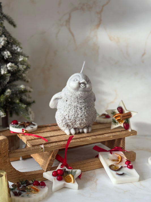 Decorative scene with a stone Pinguin on a wooden bench, surrounded by Christmas ornaments.